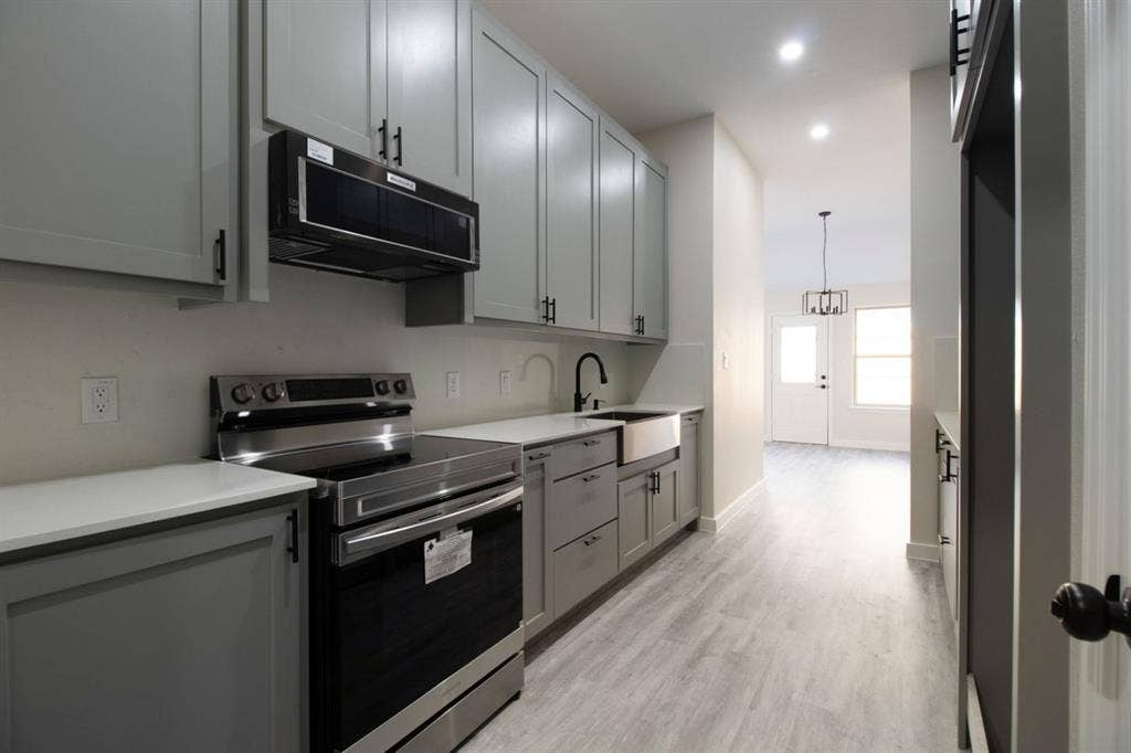 Kitchen featuring light gray cabinetry, stainless steel appliances, white countertops, and a farmhouse sink