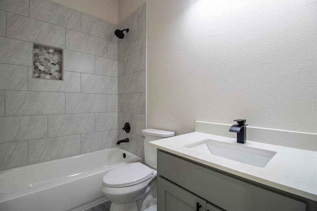 Bathtub with tiled surround and integrated niche, matte black fixtures, vanity with integrated sink, and white countertop