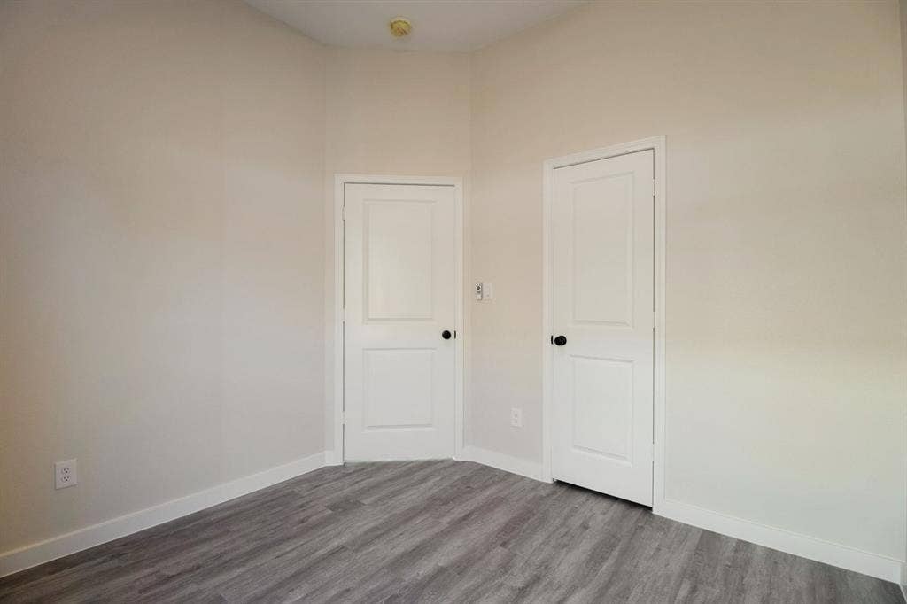Light-toned walls, two panel doors with matte black hardware, and wood-finish flooring