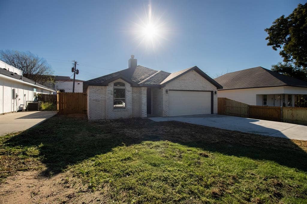 Light brick exterior, arched window, attached garage, concrete driveway, wood privacy fence