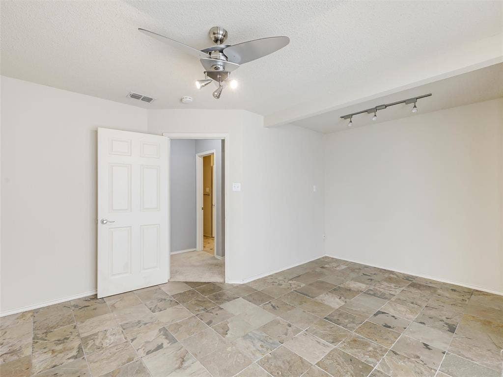 Interior space featuring multi-tonal stone tile flooring, a modern brushed-metal ceiling fan with integrated lighting, and a multi-head track lighting fixture