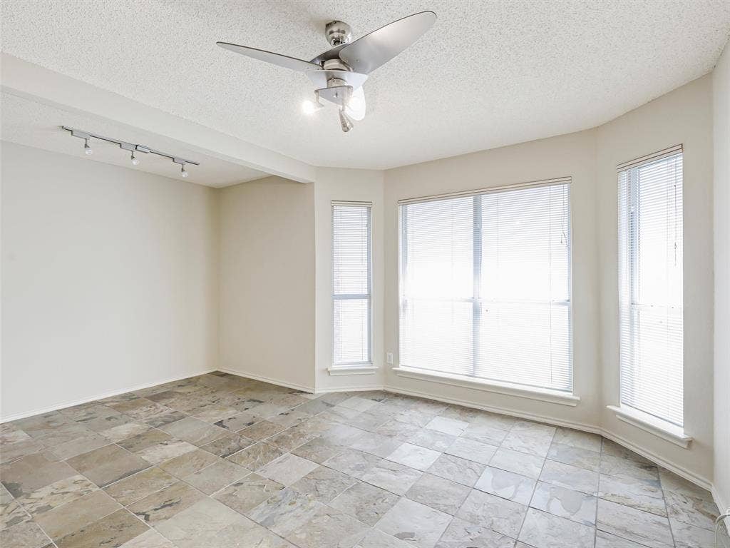 Multi-paneled bay windows, large-format tile flooring, polished metal ceiling fan with integrated light fixture, and track lighting system