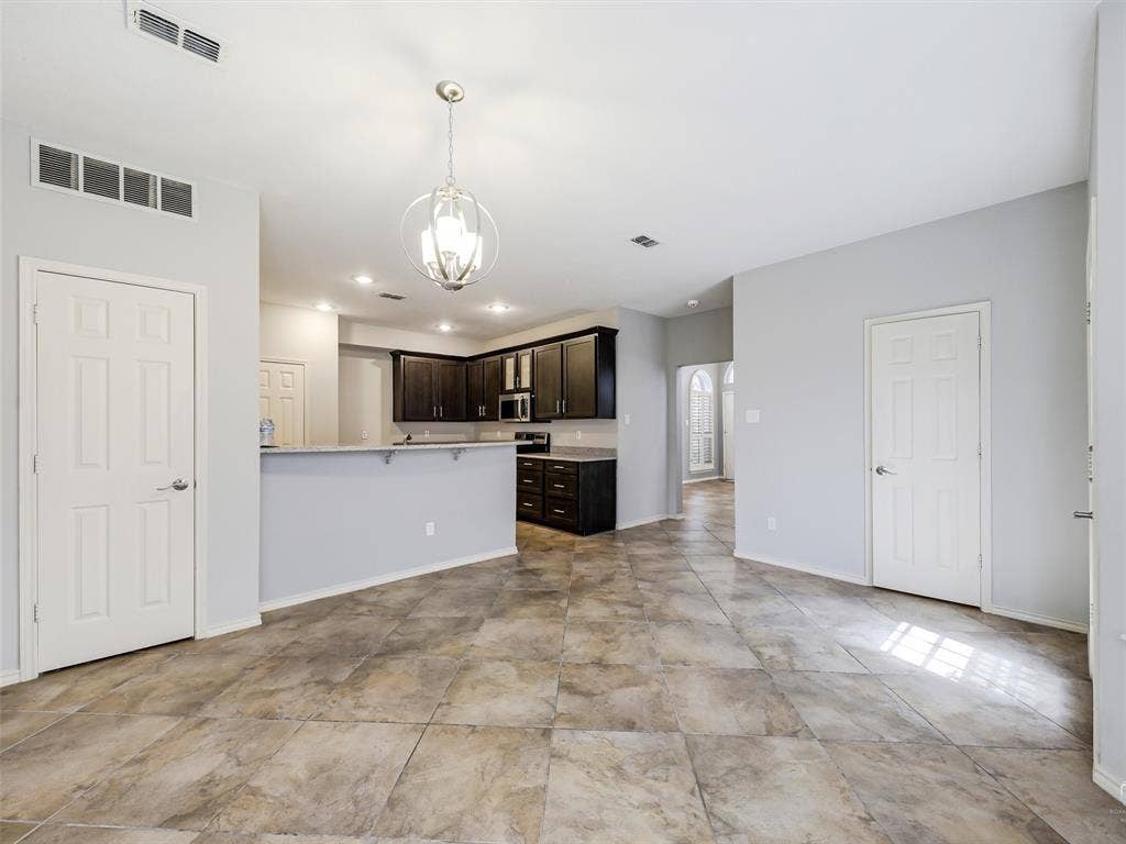 Kitchen featuring dark cabinetry, stone-finish countertops, a tiered breakfast bar, and a brushed nickel pendant light fixture, complemented by tile flooring