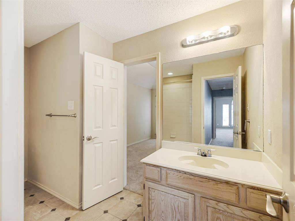 Bathroom featuring a wood-finish vanity with an integrated basin, a large wall-mounted mirror, overhead vanity lighting, and ceramic tile flooring with decorative inlay accents