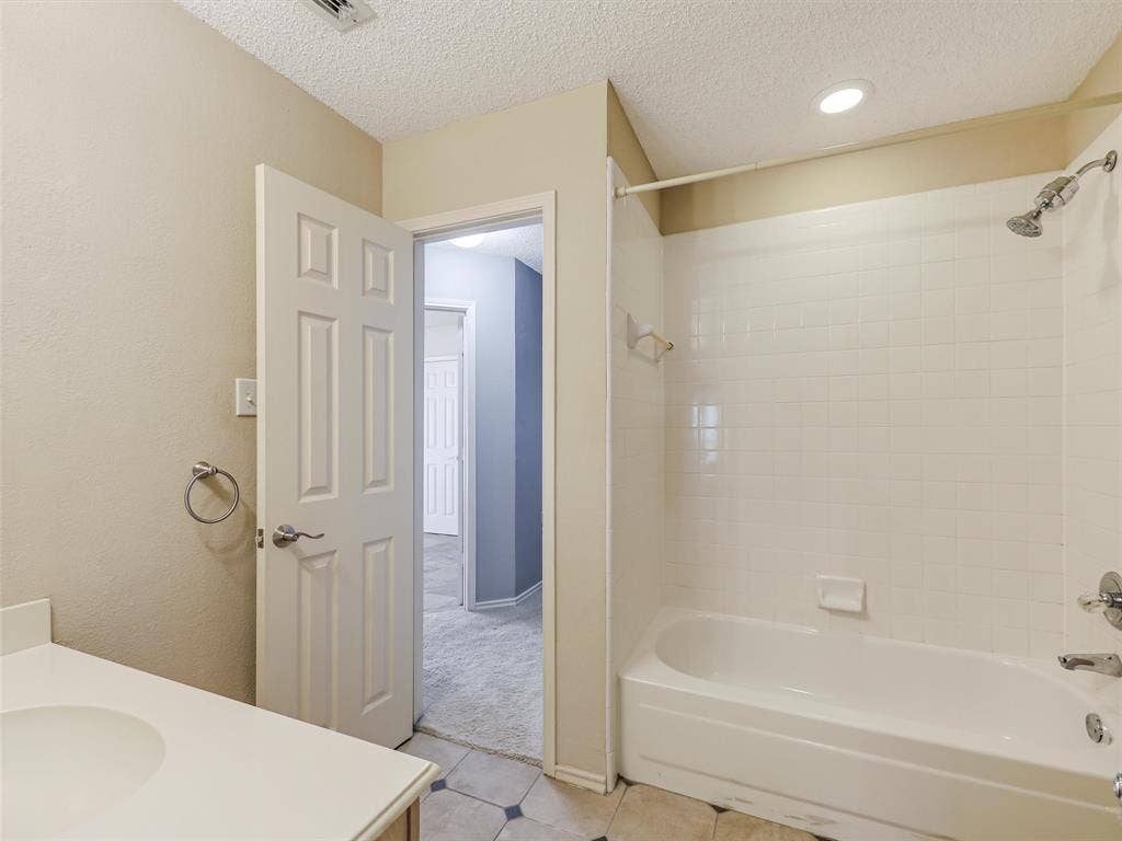 Bathroom featuring a tub-shower combination with white tile surround, recessed lighting, and a single-basin vanity