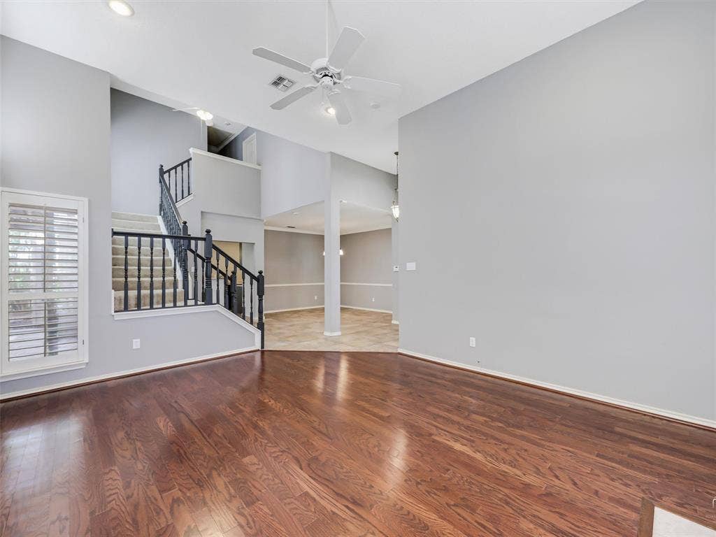 High-ceiling interior featuring wood-finish flooring, a staircase with black metal balusters, shuttered windows, and recessed lighting
