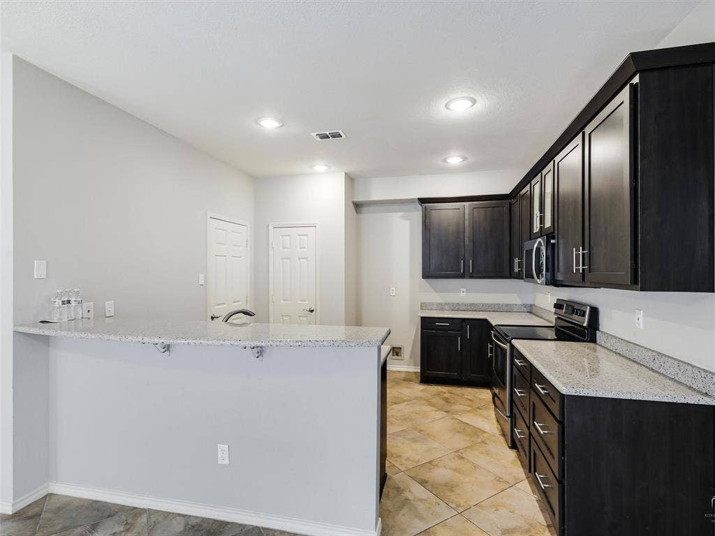 Kitchen featuring dark wood-finish cabinetry, speckled solid-surface countertops, a breakfast bar, tile flooring, and recessed lighting