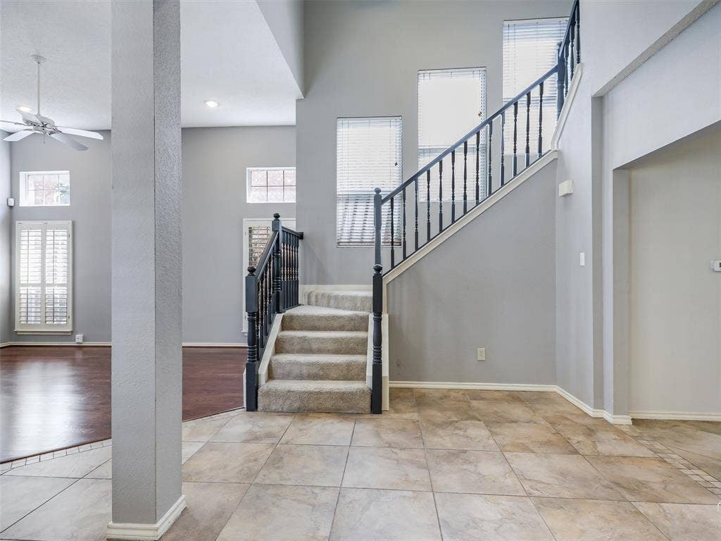 High-ceiling foyer featuring tile flooring, a staircase with a dark wood-finish railing, multi-pane windows, and inset ceiling lighting