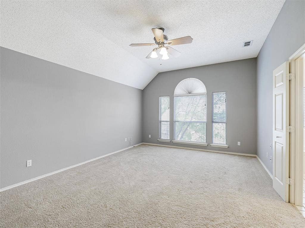 Vaulted ceilings with a ceiling fan, carpeted flooring, and a multi-pane window configuration featuring an arched transom