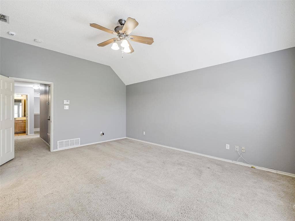 Spacious room featuring vaulted ceilings, neutral wall tones, wall-to-wall carpeting, and a ceiling fan with integrated light fixture