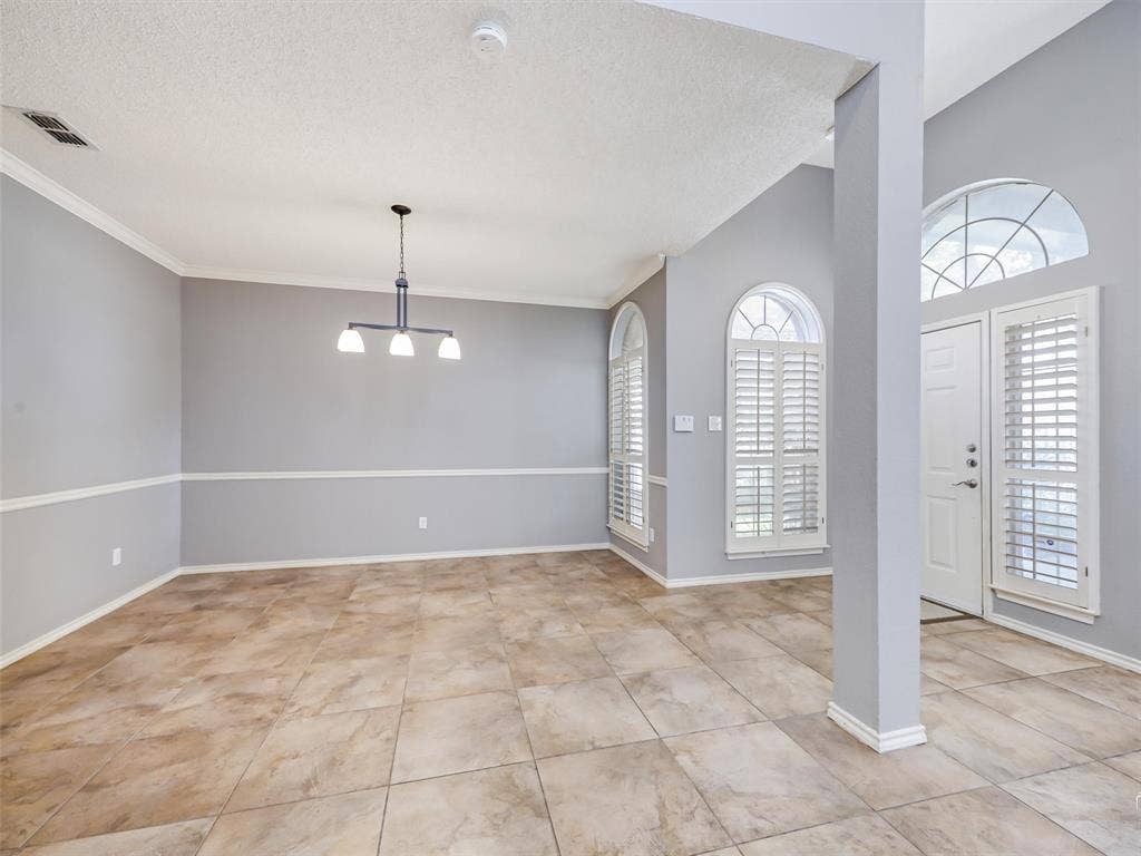 Open-concept space featuring large-format tile flooring, chair rail molding, arched windows with plantation shutters, and a central modern chandelier