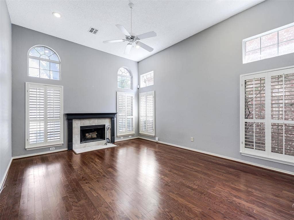 Vaulted ceilings, wood-finish flooring, fireplace with a tile surround, shutter-style window coverings, and arched windows