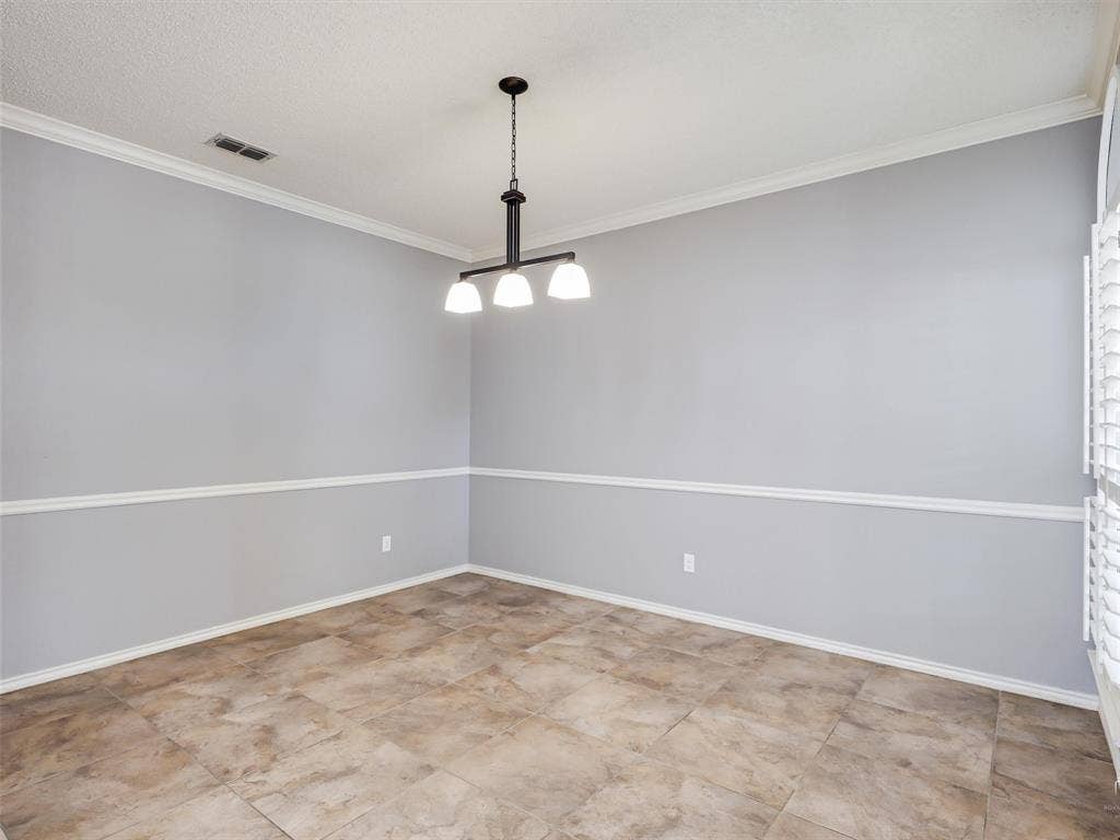 Interior room featuring tile flooring, neutral wall paint with white chair rail molding, and a three-light chandelier with a matte finish