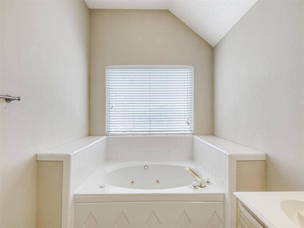 Built-in soaking tub with a tiled deck, jetted basin, and deck-mounted faucet, set within a recessed alcove beneath a window