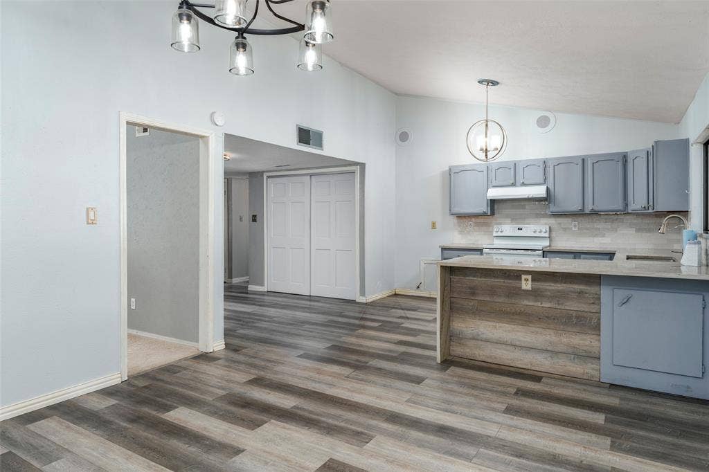 826 Camino Court, Grand Prairie, TX 75052 Kitchen featuring wood-finish flooring, a wood-paneled peninsula, slate-toned cabinetry, light-toned countertops, and multi-light pendant fixtures