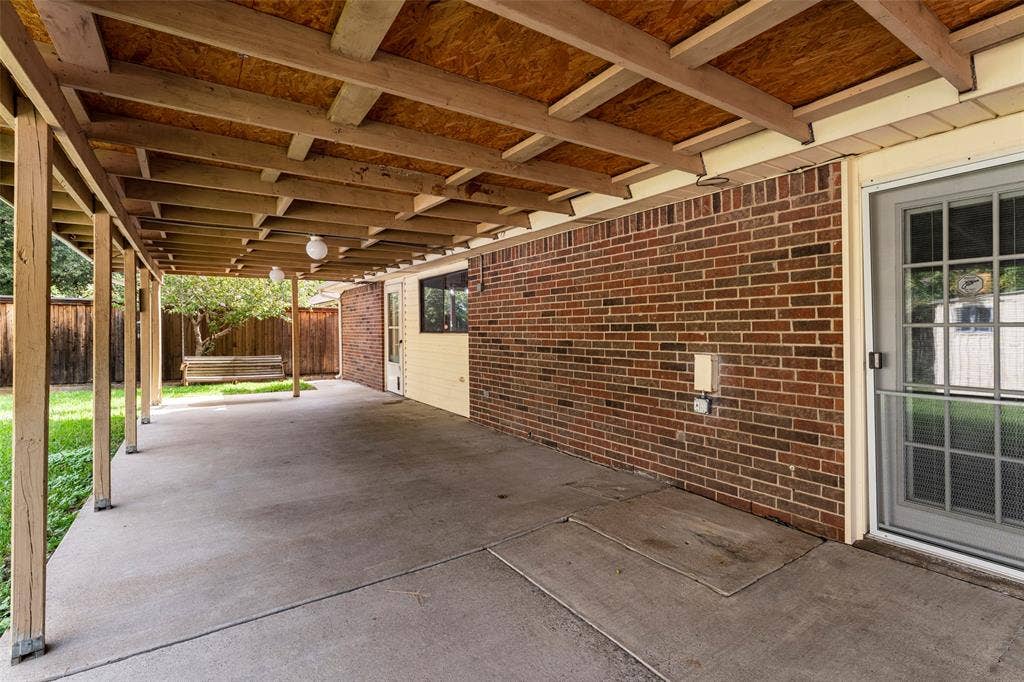 826 Camino Court, Grand Prairie, TX 75052 Covered concrete patio featuring a brick exterior wall, wood-frame ceiling structure, and integrated lighting fixtures