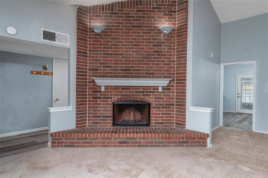 826 Camino Court, Grand Prairie, TX 75052 Floor-to-ceiling brick fireplace featuring a built-in hearth, prominent mantel, and dual wall-mounted light fixtures, set within a vaulted ceiling space