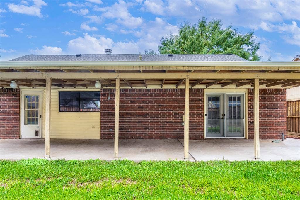 826 Camino Court, Grand Prairie, TX 75052 Covered rear patio featuring a concrete floor, red brick exterior, light-colored siding, and dual glass-panel doors