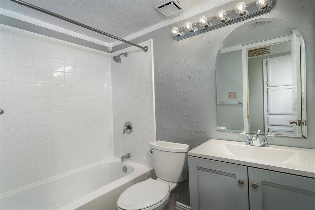 826 Camino Court, Grand Prairie, TX 75052 Bathroom featuring a white tile tub surround, arched wall-mounted mirror, vanity with a rectangular basin, and a multi-bulb light fixture