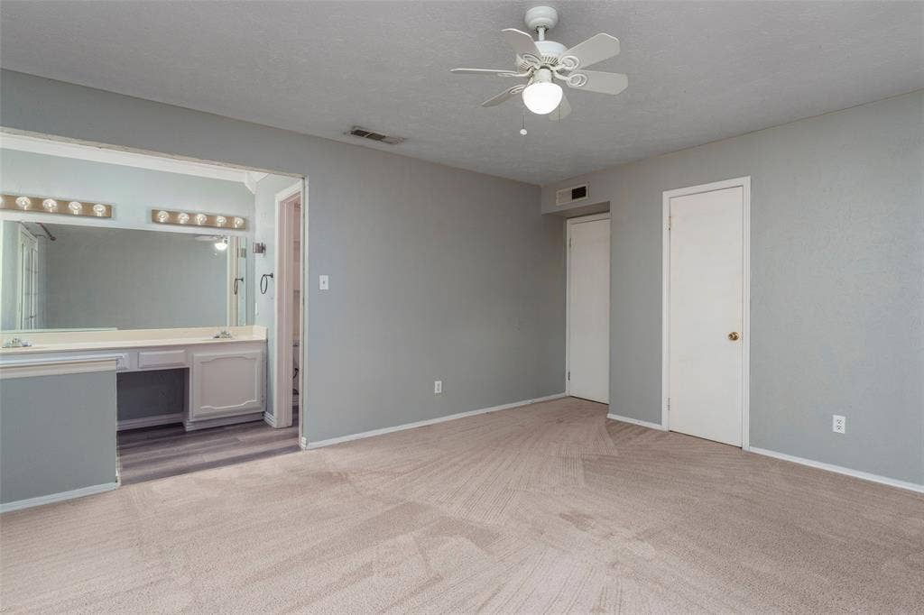 826 Camino Court, Grand Prairie, TX 75052 Neutral-toned room featuring wall-to-wall carpeting, ceiling fan with integrated lighting, dual-door closet, and an attached vanity area with a large wall mirror and multi-bulb fixture