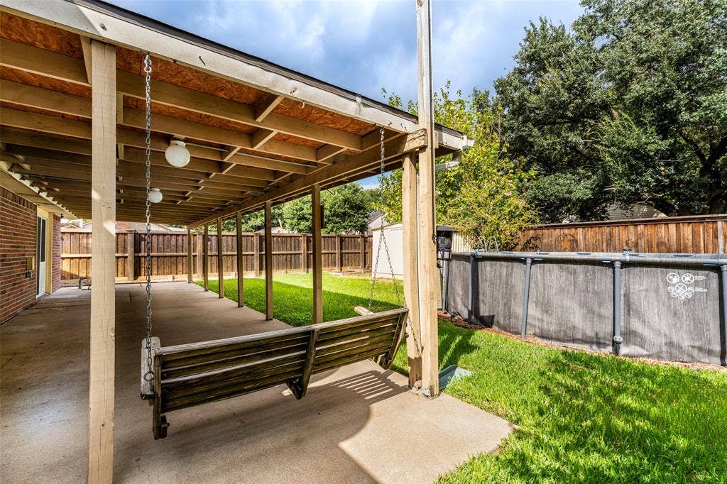 826 Camino Court, Grand Prairie, TX 75052 Covered concrete patio featuring exposed beam construction, suspended wooden bench, and fenced backyard with mature trees