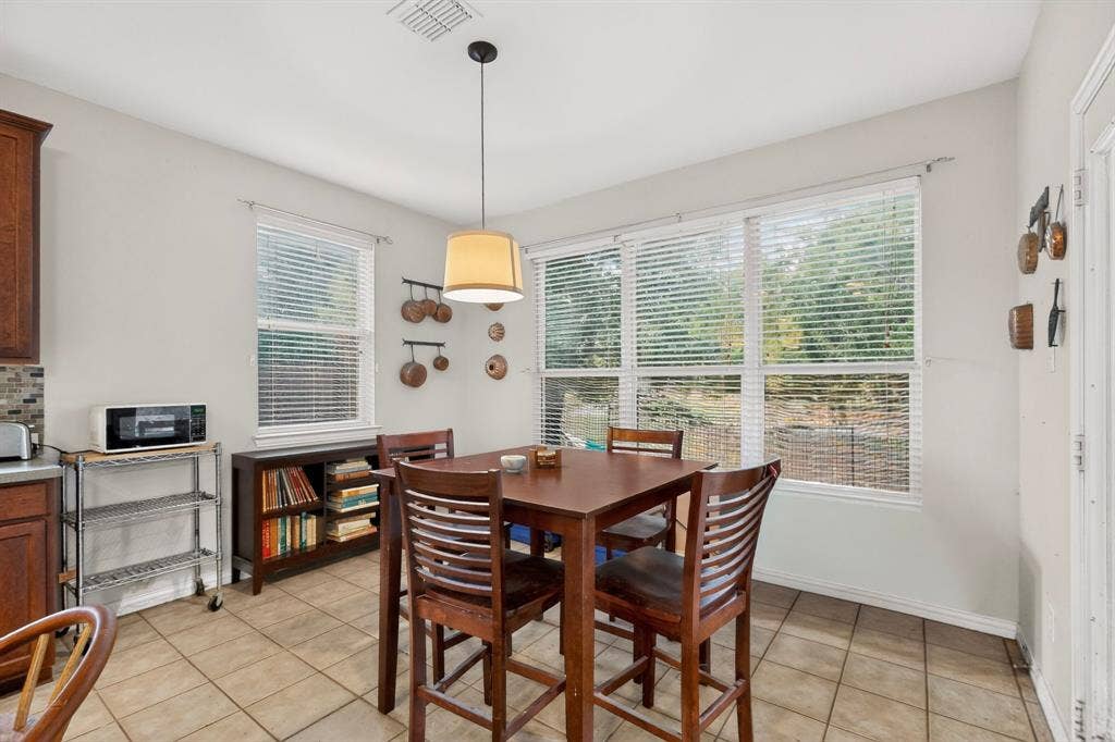 Tile flooring, oversized windows with blinds, and a drum-style pendant light fixture