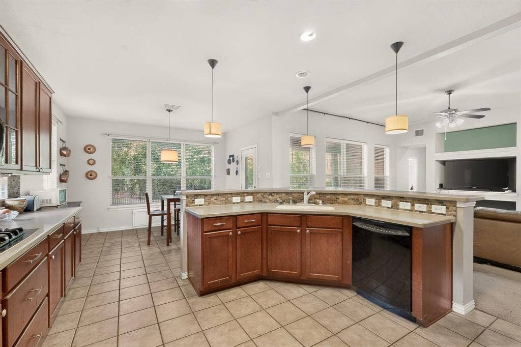 Kitchen featuring stained wood cabinetry, stone-tiled backsplash, expansive peninsula, tile flooring, and multi-pendant lighting