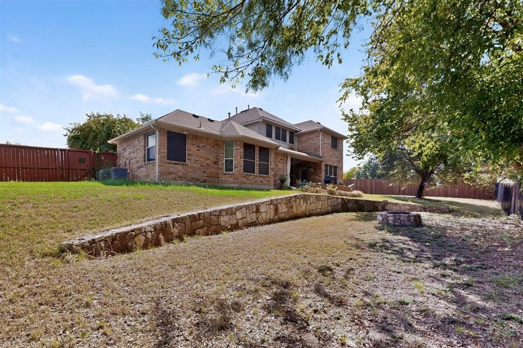 Rear exterior featuring brick siding, a multi-level stone retaining wall, built-in stone fire pit, and privacy wood fencing