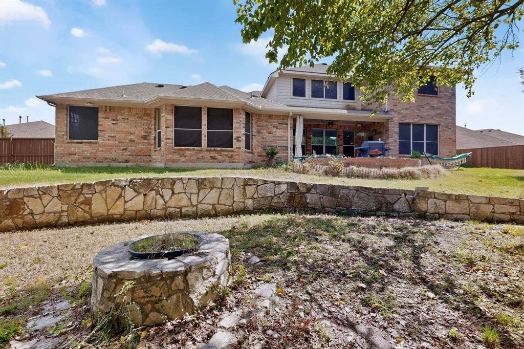 Multi-level brick exterior featuring a stone-clad fire pit, tiered stone retaining wall, and fenced backyard
