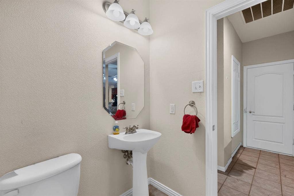 downstairs powder bath with Pedestal sink with a polished metal faucet, octagonal wall mirror, and three-light vanity fixture