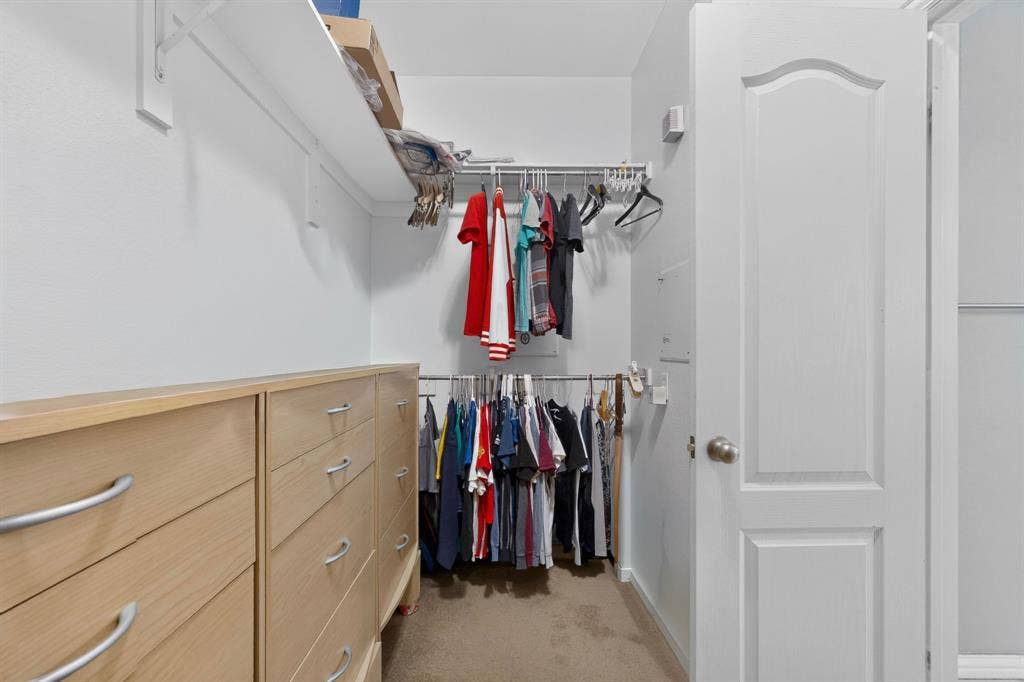 master Walk-in closet featuring built-in light wood-finish drawer units with curved metal hardware, dual-level wire shelving, and a six-panel interior door