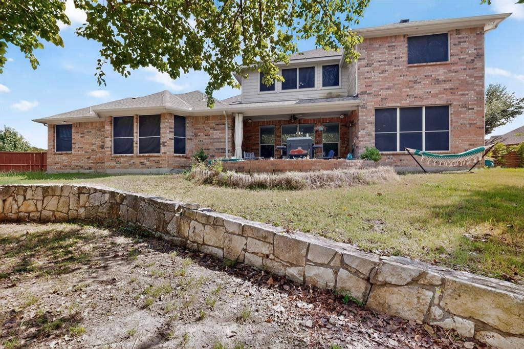 Two-story brick exterior featuring a multi-level stone retaining wall, a paved patio, and dual-material facade consisting of masonry and horizontal siding