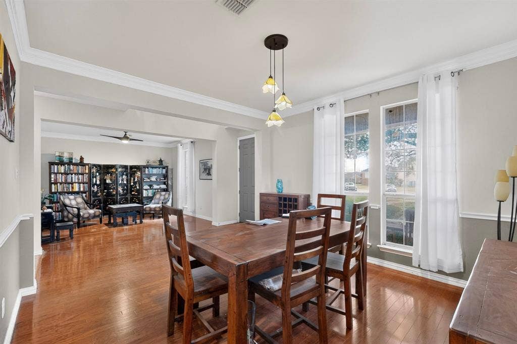 Dining area featuring wood-finish flooring, crown molding, chair rail trim, and a multi-light pendant fixture