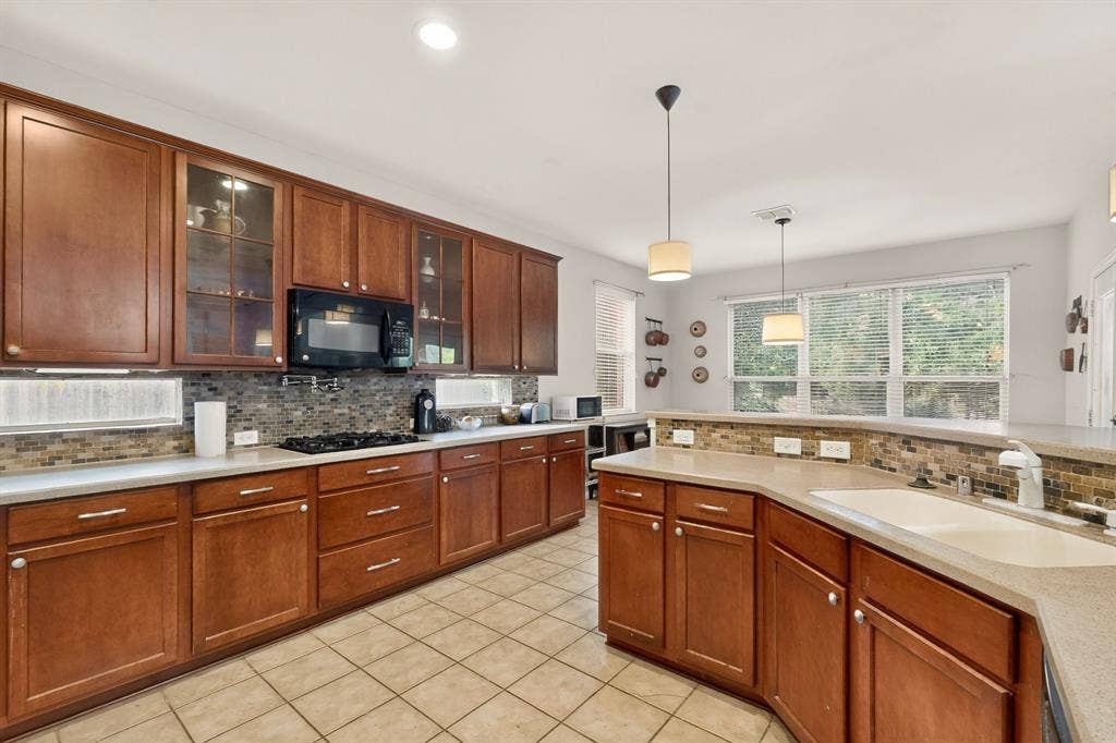 Kitchen featuring shaker-style wood cabinetry, mosaic tile backsplash, solid-surface countertops, dual-basin sink, and pendant lighting