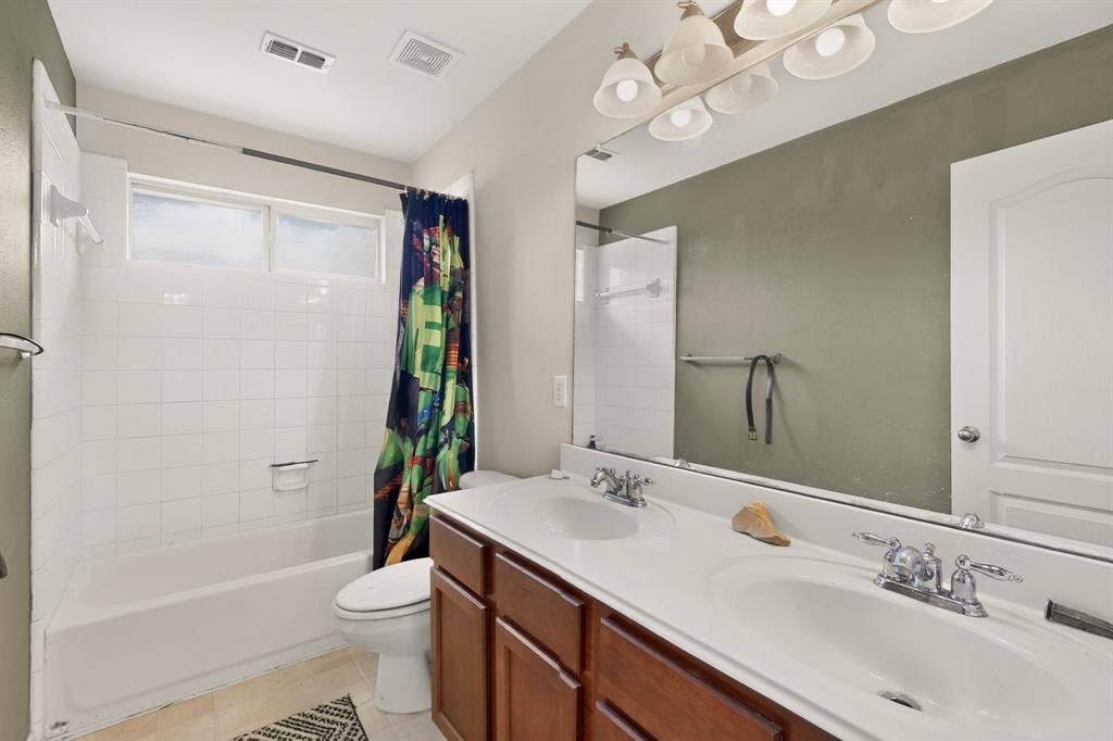 Bathroom featuring a dual-sink vanity with white countertops, expansive wall-mounted mirror, tub-shower combination with white tile surround, and polished chrome fixtures