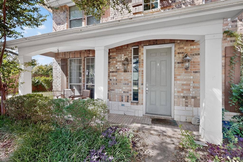Brick exterior featuring a covered front porch, stone foundation detailing, arched structural columns, and classic window shutters