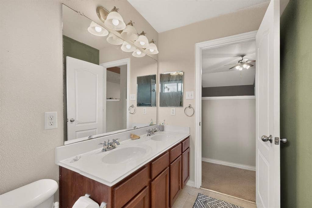 Dual-sink vanity with wood-finish cabinetry, solid-surface countertop, full-width wall mirror, and multi-bulb vanity lighting