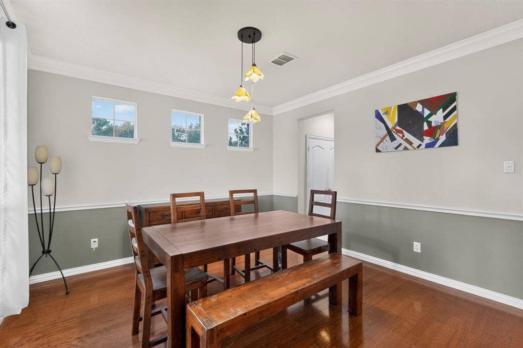 Neutral two-tone wall paint with chair rail molding, wood-finish flooring, crown molding, and multi-light hanging pendant fixture