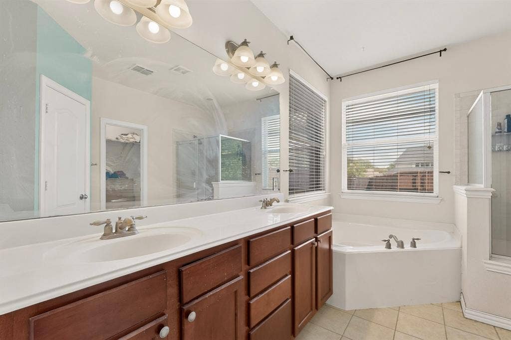 Dual-sink vanity with wood-finish cabinetry, solid-surface countertop, full-width mirror, soaking tub, and separate enclosed shower