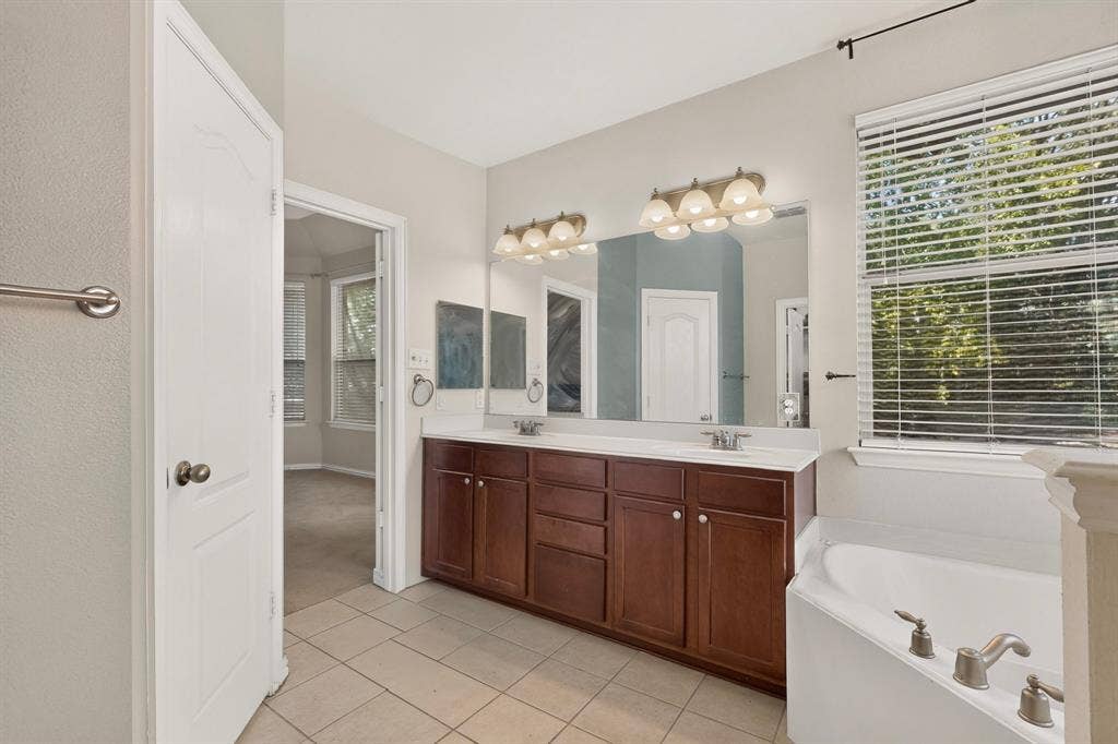 Double vanity with wood-finish cabinetry, solid-surface countertop, dual drop-in sinks, large wall-mounted mirror, and tile flooring