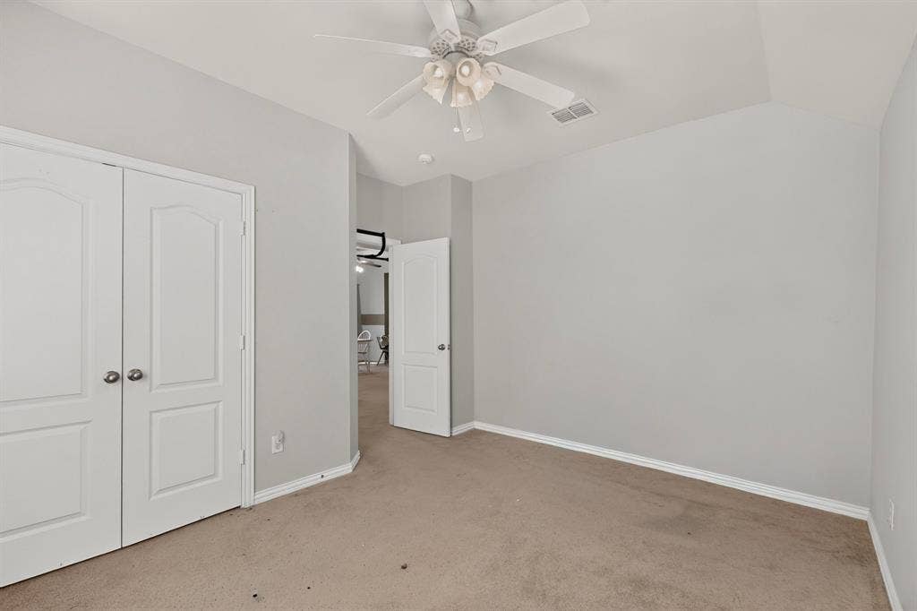 Room featuring vaulted ceilings, neutral-toned carpeting, two-panel interior doors, and a multi-blade ceiling fan with integrated lighting