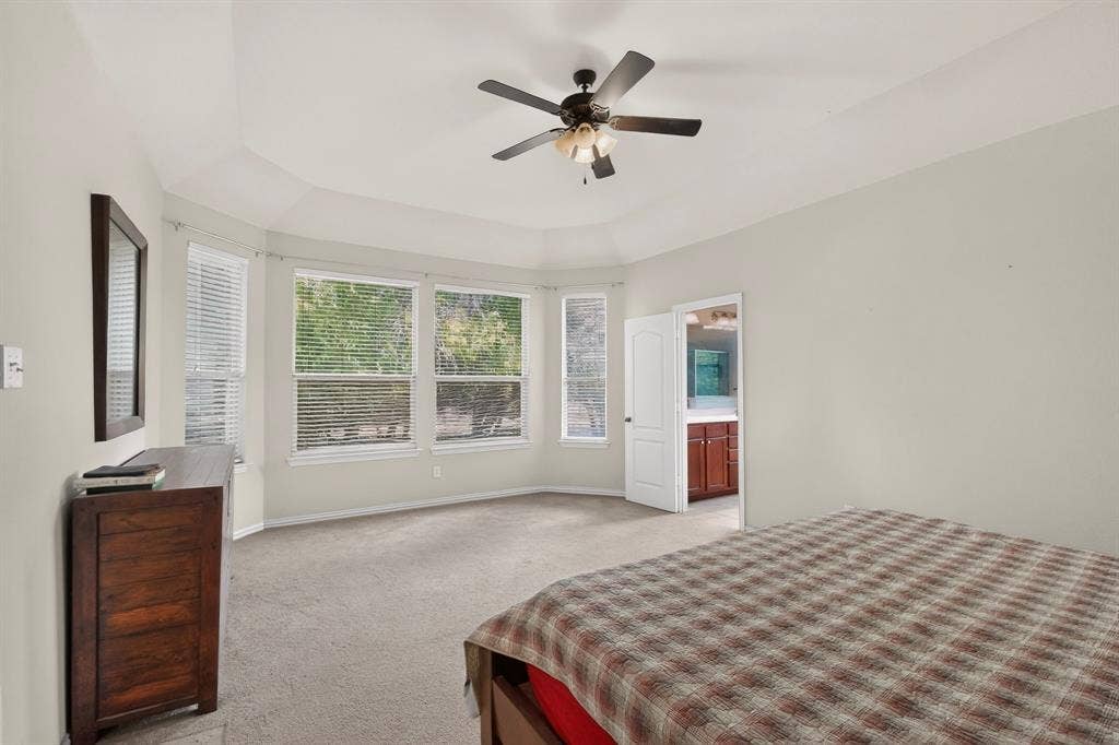 Bedroom featuring a tray ceiling, ceiling fan with light fixture, neutral wall color, carpeting, and bay windows
