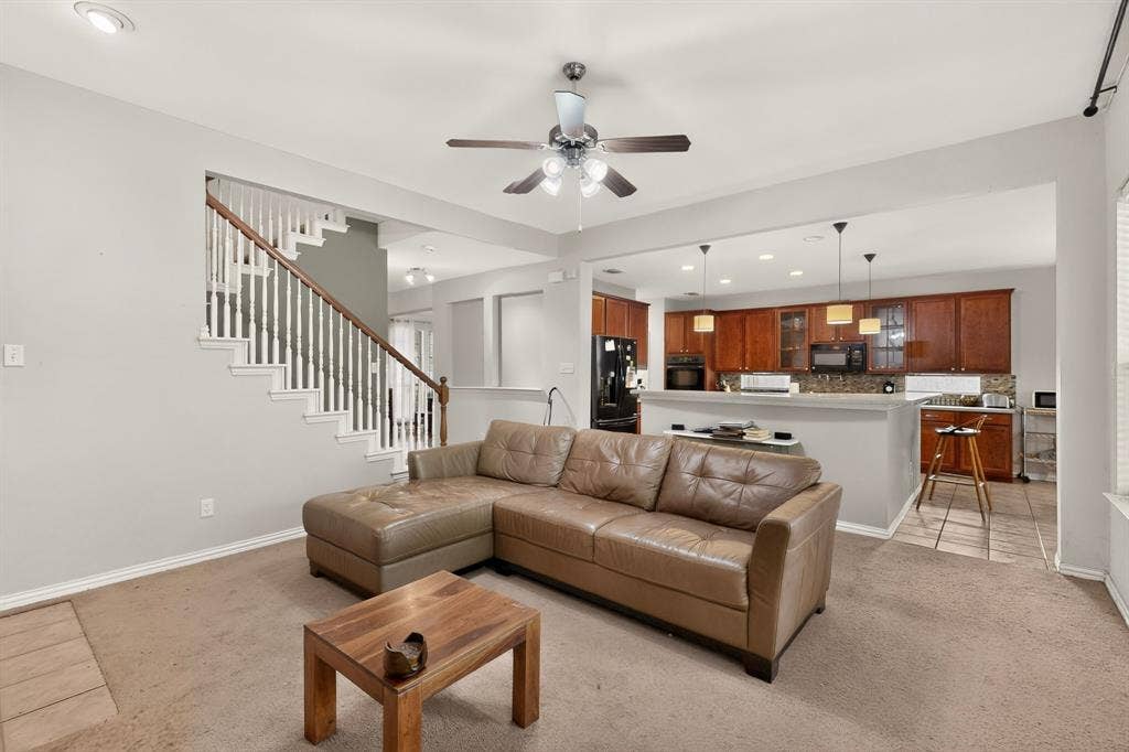 Open-concept living space featuring wood-finish cabinetry, a raised breakfast bar, recessed lighting, and a staircase with a wooden handrail and balusters