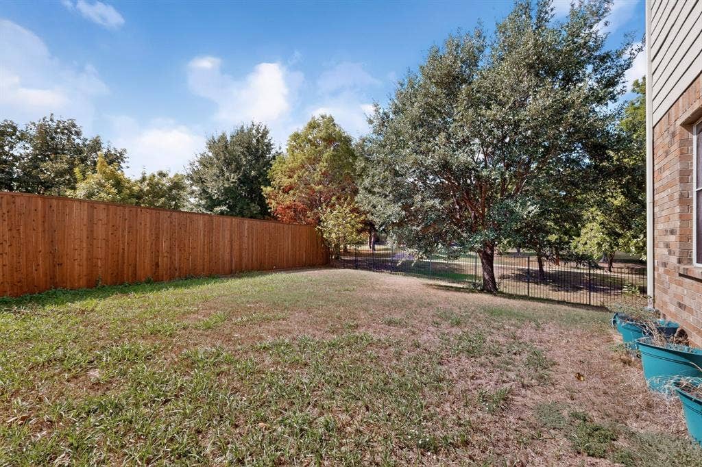 Private backyard featuring a wood privacy fence, decorative metal perimeter fencing, mature trees, and brick exterior cladding