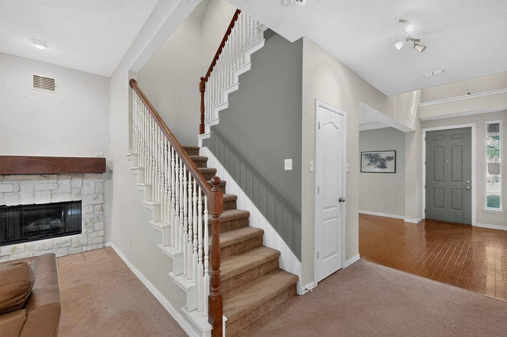 Interior featuring a stone-surround fireplace with a wooden mantel, a staircase with white balusters and a wood-finish handrail, and high-gloss wood-finish flooring