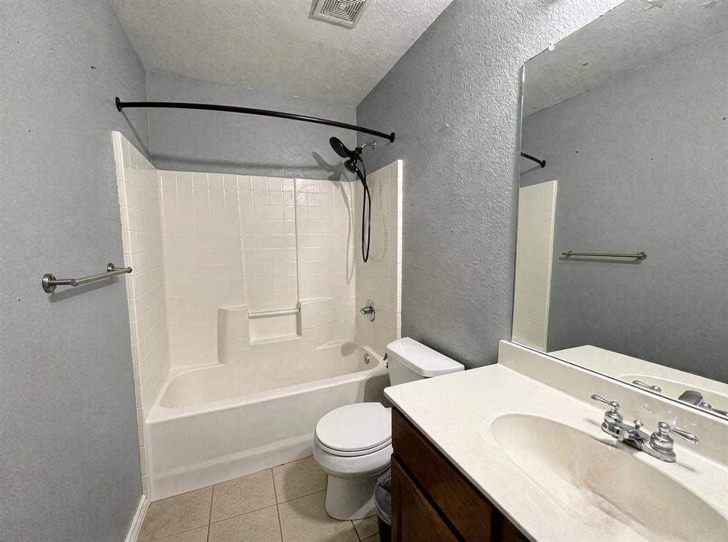 Bathroom featuring a vanity with an integrated sink, white composite tub and shower surround, wall-mounted mirror, and ceramic tile flooring