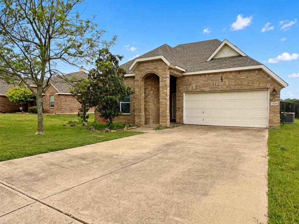 Single-story brick exterior featuring a recessed arched entryway, attached two-car garage, and a concrete driveway