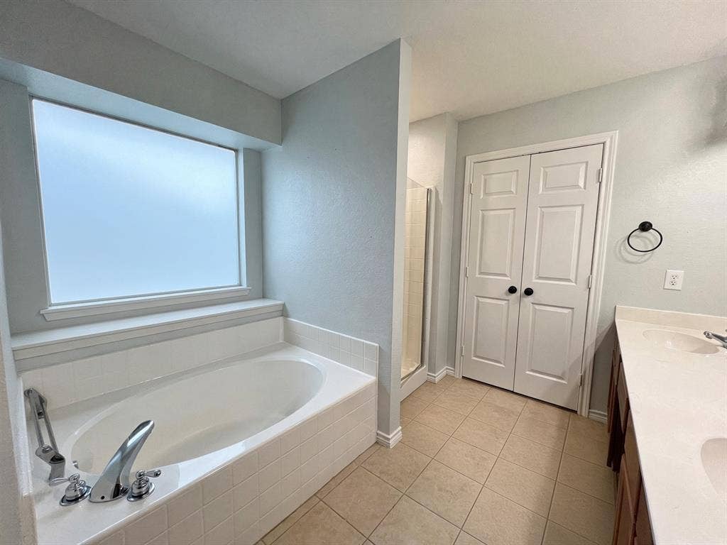 Bathroom featuring a tile-surround soaking tub, frosted window, double-door closet, tiled flooring, and dual-sink vanity