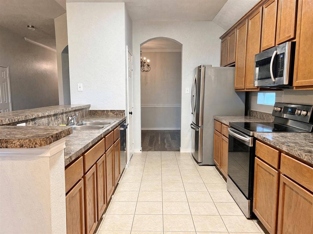 Kitchen featuring wood cabinetry, stainless steel appliances, laminate countertops, and ceramic tile flooring