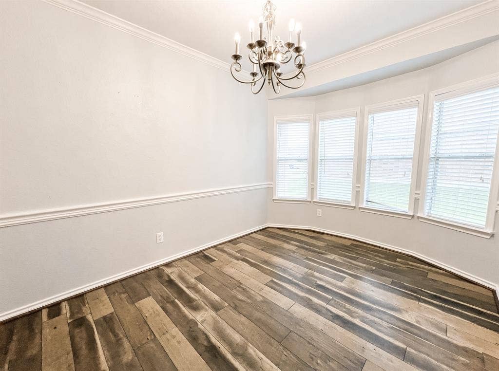 Wood-finish flooring, bay window, crown molding, chair rail, and decorative chandelier
